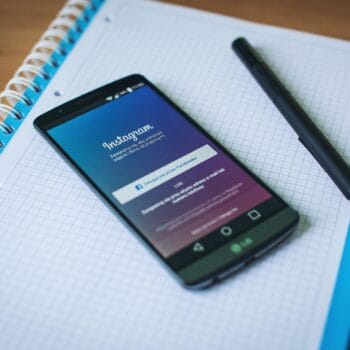 Un telefono con Instagram appoggiato su un quaderno a quadretti aperto, accanto a una penna