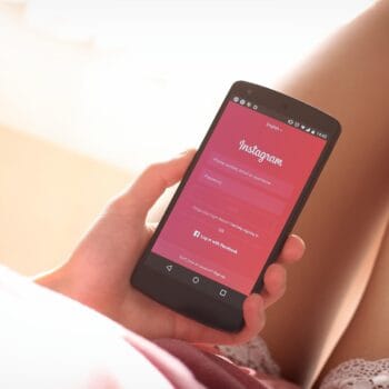 Una donna guarda lo schermo del telefono con Instagram aperto, seduta con la luce del pomeriggio