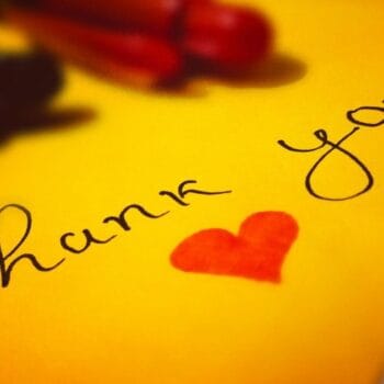 Un foglio giallo con scritto a mano thank you e un cuore rosso disegnato accanto, con due pennarelli appoggiati sopra