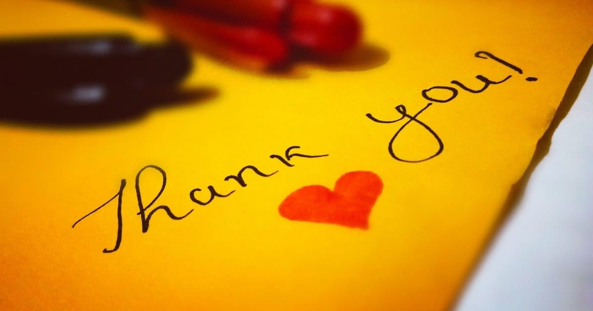Un foglio giallo con scritto a mano thank you e un cuore rosso disegnato accanto, con due pennarelli appoggiati sopra