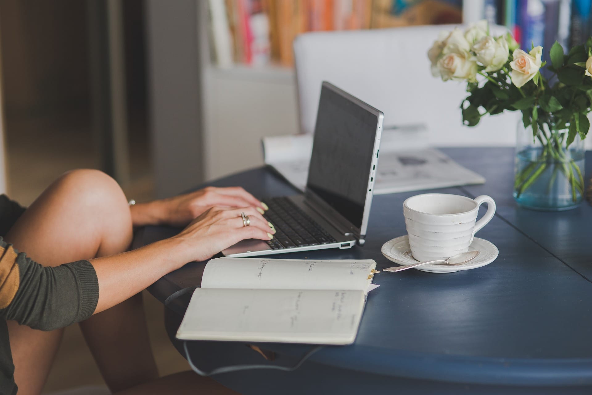 Donna che scrive appunti a mano su un quaderno accanto al computer, con una tazza di caffè sul tavolo